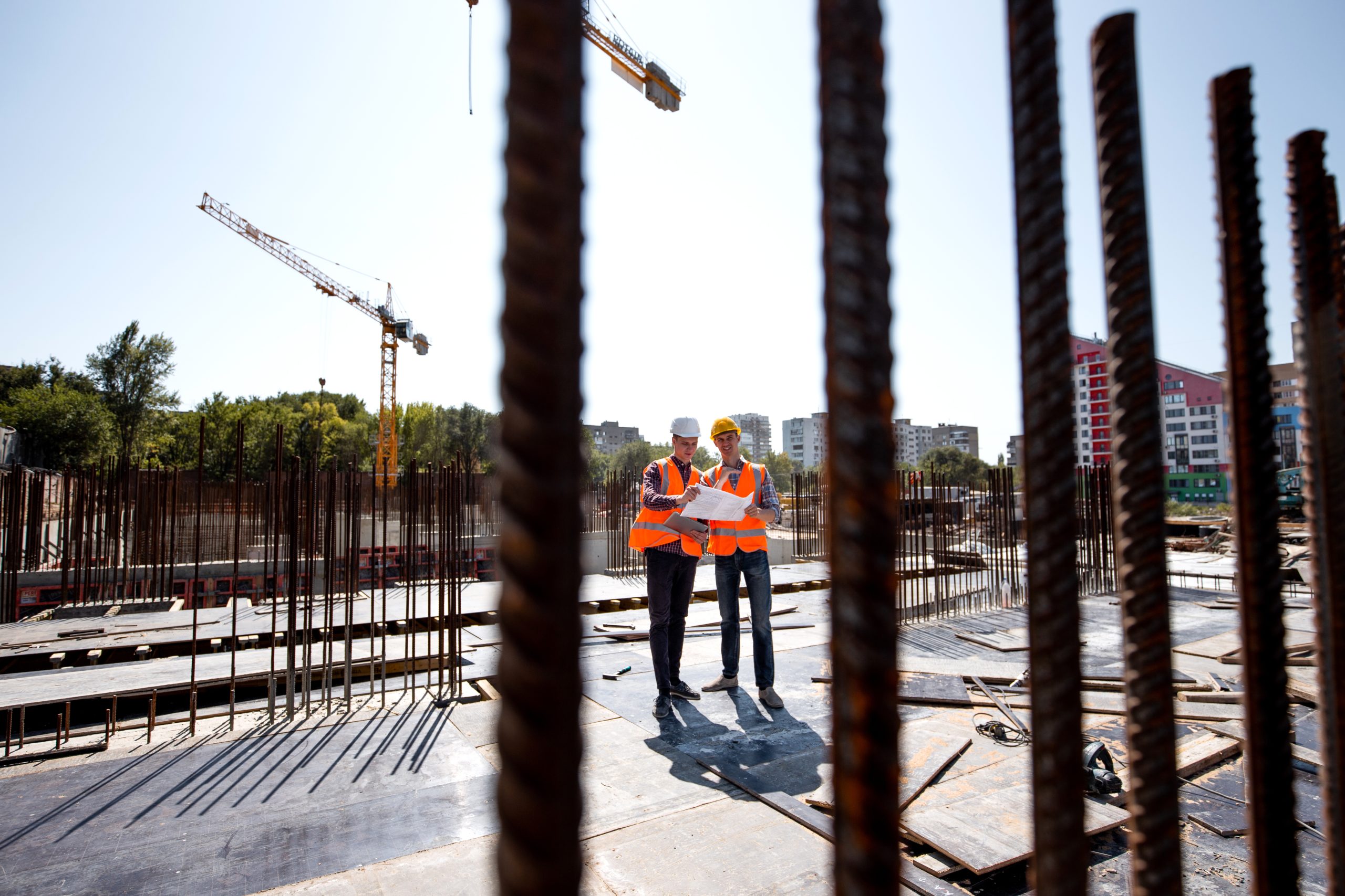 Two men dressed in shirts, orange work vests and helmets explore construction documentation on the building site near the steel frames Two men dressed in shirts, orange work vests and helmets explore construction documentation on the building site near the steel frames .